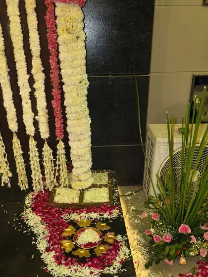 A floor-level view of a Diwali entrance decoration, showing the base of the floral arch and rangoli made of flower petals.