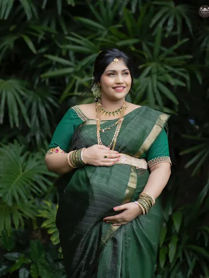 A glowing solo portrait of an expectant mother in a gorgeous green silk saree. The natural light and lush background enhance her radiant smile.