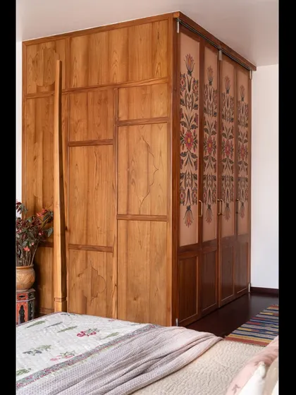A 10-foot tall, custom-built teak wardrobe with hand-painted floral details, designed to be both a functional storage solution and a beautiful piece of furniture.
