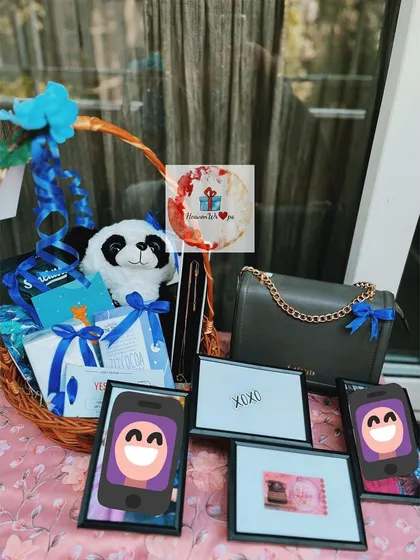 A fun and personalized birthday basket with a blue and white theme. It includes a panda soft toy, a chic handbag, and several small framed items for a unique touch.