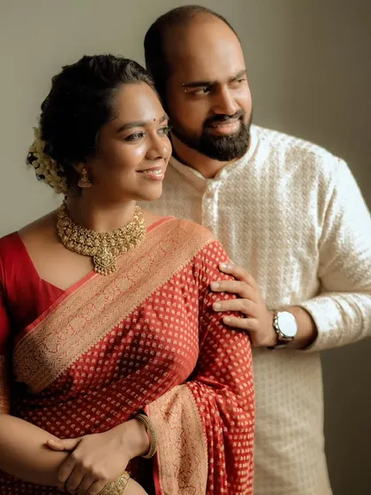 A warm and happy portrait of a couple, the bride in a red saree and the groom in a white kurta.