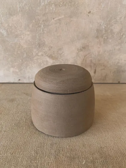 A simple, cylindrical lidded jar, unglazed to showcase the natural color and texture of the stoneware clay.