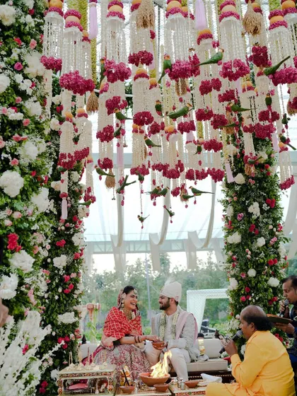 A closer look at the magnificent floral mandap, where the couple is framed by pillars wrapped in roses and a ceiling adorned with hanging tuberoses and parrots for a touch of whimsy.