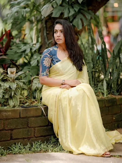 A moment of quiet elegance. This shot captures the beautiful fall of the lightweight yellow saree against a lush green background, showing its versatility and grace.
