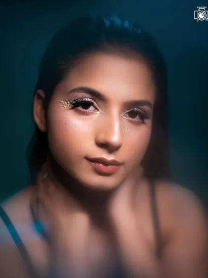 A direct and engaging beauty portrait where the model looks straight at the camera. The subtle blue tones and the gold glitter on the eyes create a beautiful contrast.