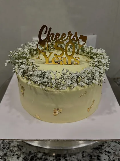 A golden anniversary celebration cake for 50 years. This design is simple yet elegant, featuring a wreath of delicate baby's breath and a custom "Cheers to 50 Years" topper.