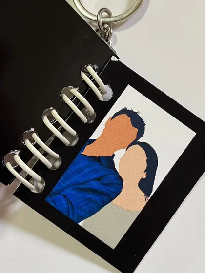 A close-up of an open booklet keychain, showing the faceless illustration inside.