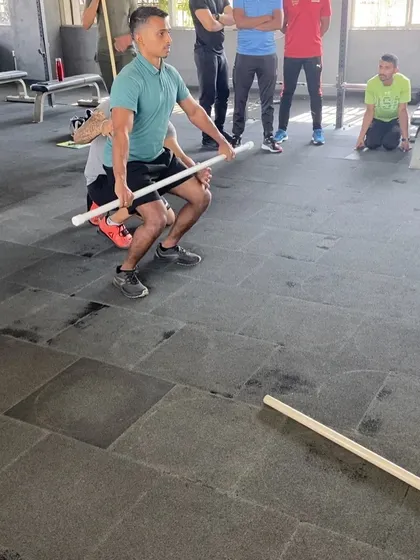 A coach practices the clean pull with a PVC pipe. We drill the fundamentals relentlessly to build a strong foundation for advanced lifting.
