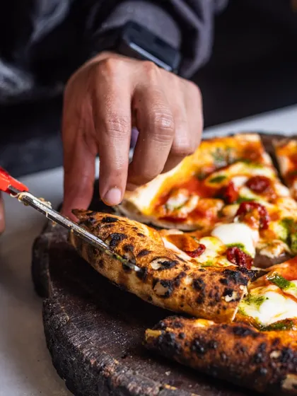 Cutting into a Sundried Tomato & Basil pizza with scissors, the traditional Italian way. This method keeps the toppings in place and prevents the crust from being squashed.