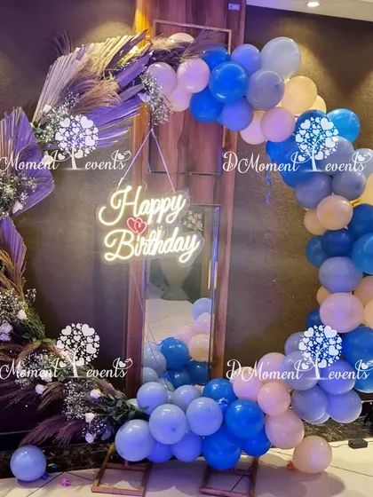 A stylish circular photo frame made of balloons and dried pampas grass, with a neon "Happy Birthday" sign for a modern touch.