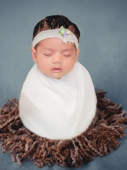 This minimalist portrait places the focus squarely on the newborn. Swaddled in white and resting on a textured brown nest, this image highlights the simple, perfect form of a sleeping baby.