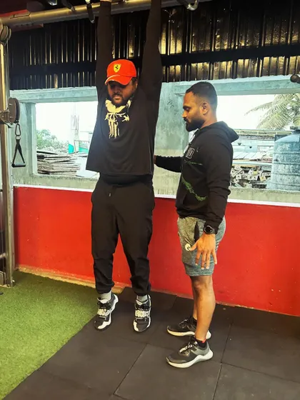 A trainer provides support and guidance as a client works on their pull-up strength.