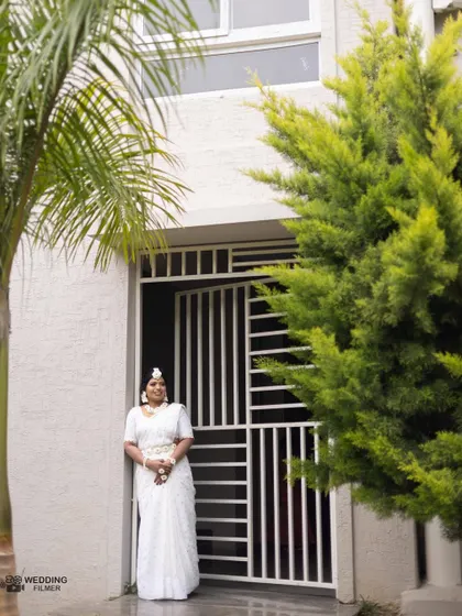 A full-length shot of the bride in her elegant white Haldi attire, standing by the entrance of her home.
