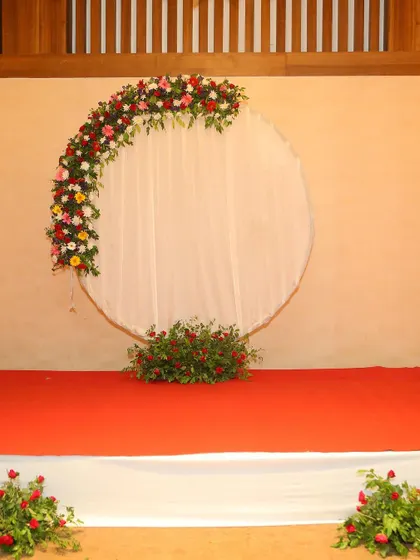 The simple yet elegant circular stage backdrop with a floral accent, set on a red carpet.
