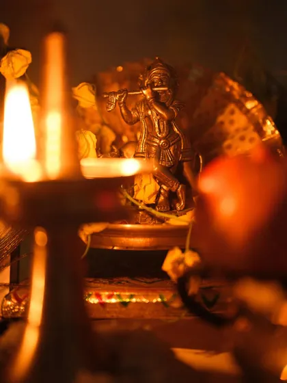 A creative shot focusing on the Krishna idol through the flame of the lamp, symbolizing divine light and blessings.
