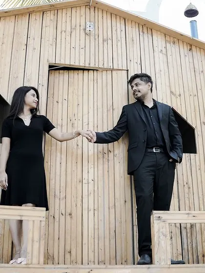 A simple, elegant pose of a couple holding hands on the porch of a rustic wooden cabin.
