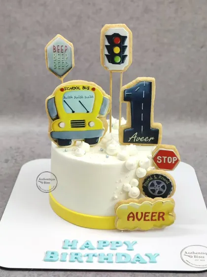 A cute school bus cake for a first birthday. This cake is decorated with cookie toppers shaped like a bus, traffic lights, and road signs.