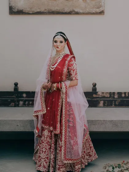 A full-length portrait of the bride in her traditional red lehenga. Her pose is graceful and poised, a perfect picture of a classic Indian bride.