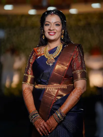 A full portrait of the bride in her engagement attire. The makeup is designed to complement her beautiful navy and rust-colored saree and traditional gold jewellery.