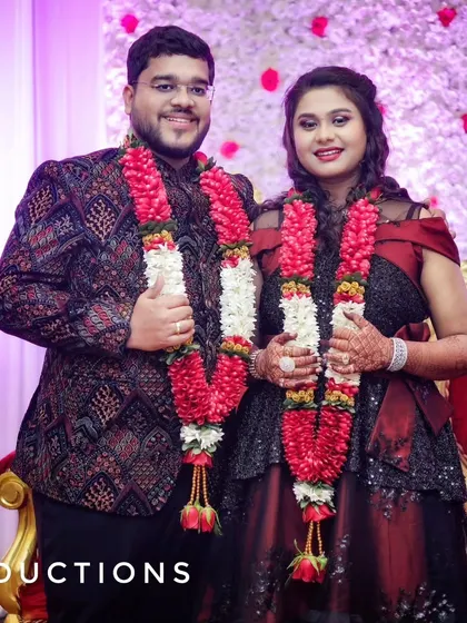 A formal portrait of the newly engaged couple, smiling together and wearing beautiful red floral garlands.