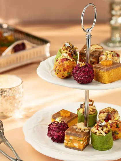 An assortment of modern Indian mithai elegantly displayed on a two-tiered stand. This image for Marriott Bonvoy showcases the variety and beauty of their Diwali collection, presented like a festive high tea.