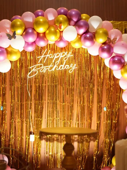 A close-up of a 'Happy Birthday' neon sign against a gold shimmer backdrop from a butterfly party.