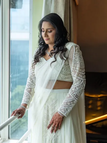 A contemplative moment by the window. The natural light highlights the soft waves in her hair and the flawless finish of her makeup.