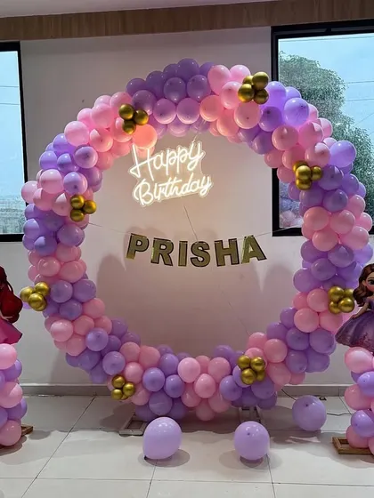 A princess-themed birthday party featuring a full circular balloon arch in pink and purple. The setup is flanked by balloon pillars with princess cutouts.