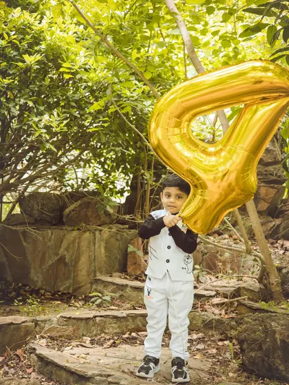 A portrait of the fourth birthday boy posing with his giant gold balloon. The natural, rocky background adds a great texture to the photo.