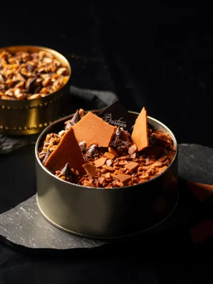 A deconstructed tiramisu-style dessert in a tin from Bastian. The dark, moody lighting and sharp textures create a sophisticated and modern dessert portrait.