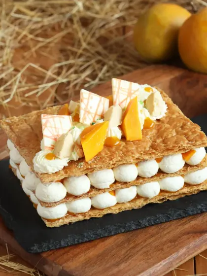 A rectangular Mango Mille-feuille, showcasing the flaky layers of puff pastry and dollops of fresh cream, all topped with sweet mango pieces.
