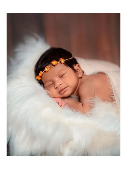 A close-up of a sleeping newborn resting on a fluffy white fur blanket.