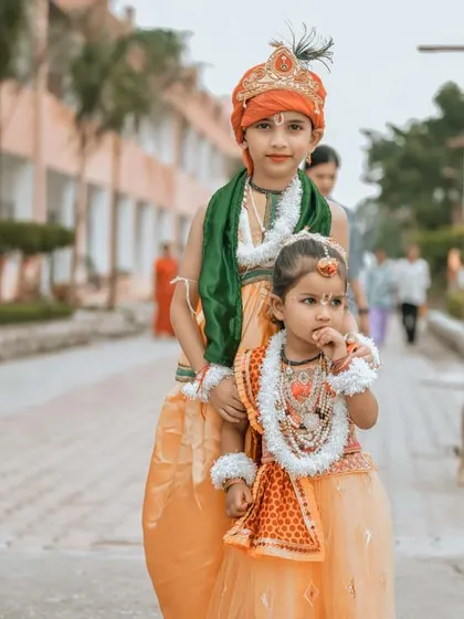 A full-length portrait of two children dressed as the divine couple Radha and Krishna. This photo captures their innocent expressions and traditional attire against the backdrop of Hanuman Dham in Jim Corbett.