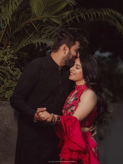 A tender forehead kiss in the evening light. This intimate moment, captured against a backdrop of city lights and foliage, is both romantic and modern.