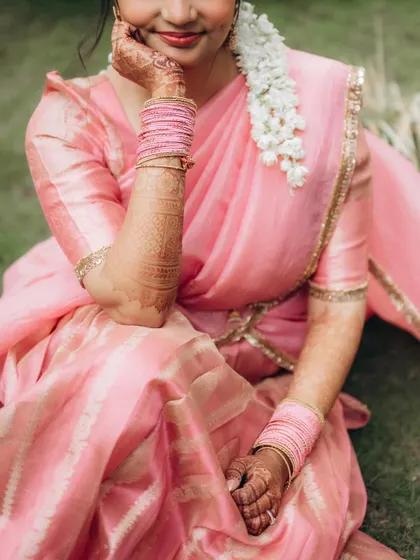 A close-up portrait of the bride, Dhriti, showcasing her beautiful pink saree, intricate henna, and the delicate gajra in her hair.