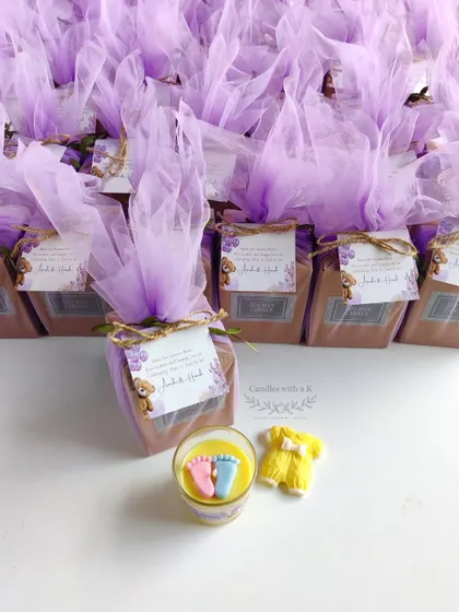 A baby shower gift set including a baby feet votive candle and a baby onesie wax sachet, all beautifully packaged for Amishi and Harsh's celebration.
