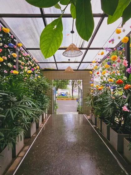 The entrance to a cafe, transformed into a floral wonderland for a baby shower. The pathway is lined with lush plants and hanging flowers, creating a secret garden feel.