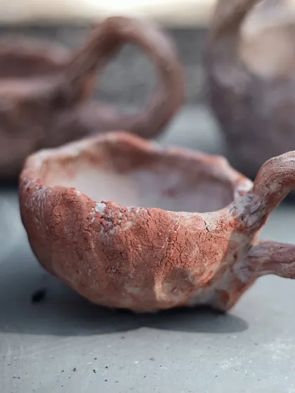 A close-up of a hand-built cup, showing the raw, textured surface and the organic shape of the handle. This is the beauty of handmade.