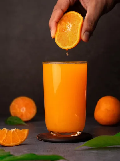 A more dramatic take on orange juice, with a hand squeezing a fresh orange into the glass. The dark background makes the orange color stand out, adding a dynamic and fresh feel to the image.