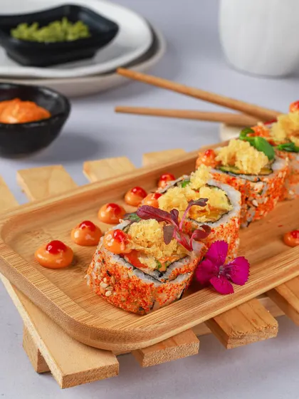 Tempura crunch sushi rolls dotted with spicy mayo, beautifully arranged on a bamboo platter.