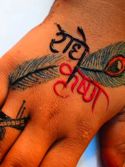 A modern and colorful take on the Radhe Krishna theme. The names are written in black and red henna, set against two peacock feathers, creating a striking design on the back of the hand.