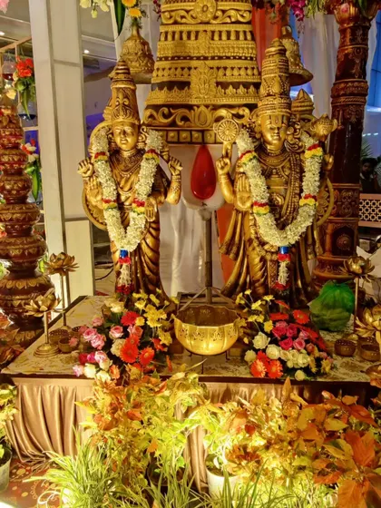 A close-up of the deity statues at the wedding entrance. The golden idols are adorned with fresh flower garlands and surrounded by lush greenery and floral arrangements.