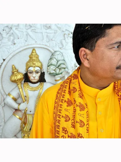 A portrait of a priest standing before a marble carving of Lord Hanuman. This photograph from the commissioned series focuses on the human element of faith within the temple.