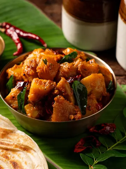 A bowl of spicy potato stir-fry (poriyal). The lighting emphasizes the texture and the rich color from the spices.