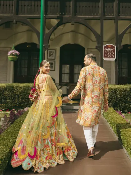 Walking hand-in-hand, this couple's coordinated Haldi outfits are a perfect match. Her colorful lehenga and his printed kurta create a cohesive and stylish look.