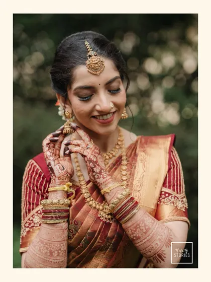 A beautiful close-up of the bride, smiling as she adjusts her bangles. This portrait highlights the intricate details of her bridal jewelry, from the Maang Tikka to the layers of necklaces and henna-adorned hands.