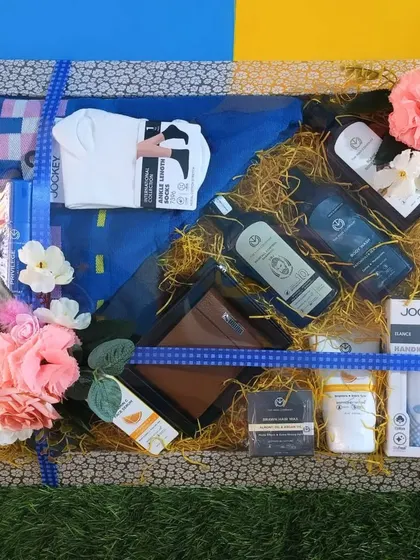 A hamper for the groom filled with daily essentials. It includes grooming products, socks, a wallet, and casual wear, all beautifully arranged on a bed of yellow shredded paper.