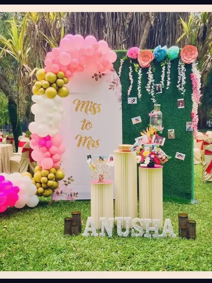 Anusha's "Miss to Mrs" bridal shower was celebrated with this lovely outdoor setup. The decor features a green hedge wall for photos, a pink and white balloon arch, and personalized details for the bride-to-be.
