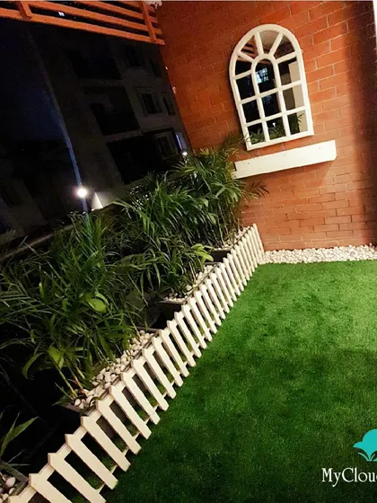 Even at night, a well-designed balcony can be a charming escape. For this space, I used artificial grass, a classic white picket fence for definition, and a decorative window mirror on the brick wall to add a touch of rustic elegance and create an illusion of more space.