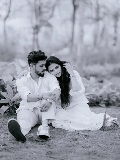 A quiet, black and white portrait of a couple sitting together in a forest. She rests her head on his shoulder, creating a feeling of comfort, peace, and togetherness.